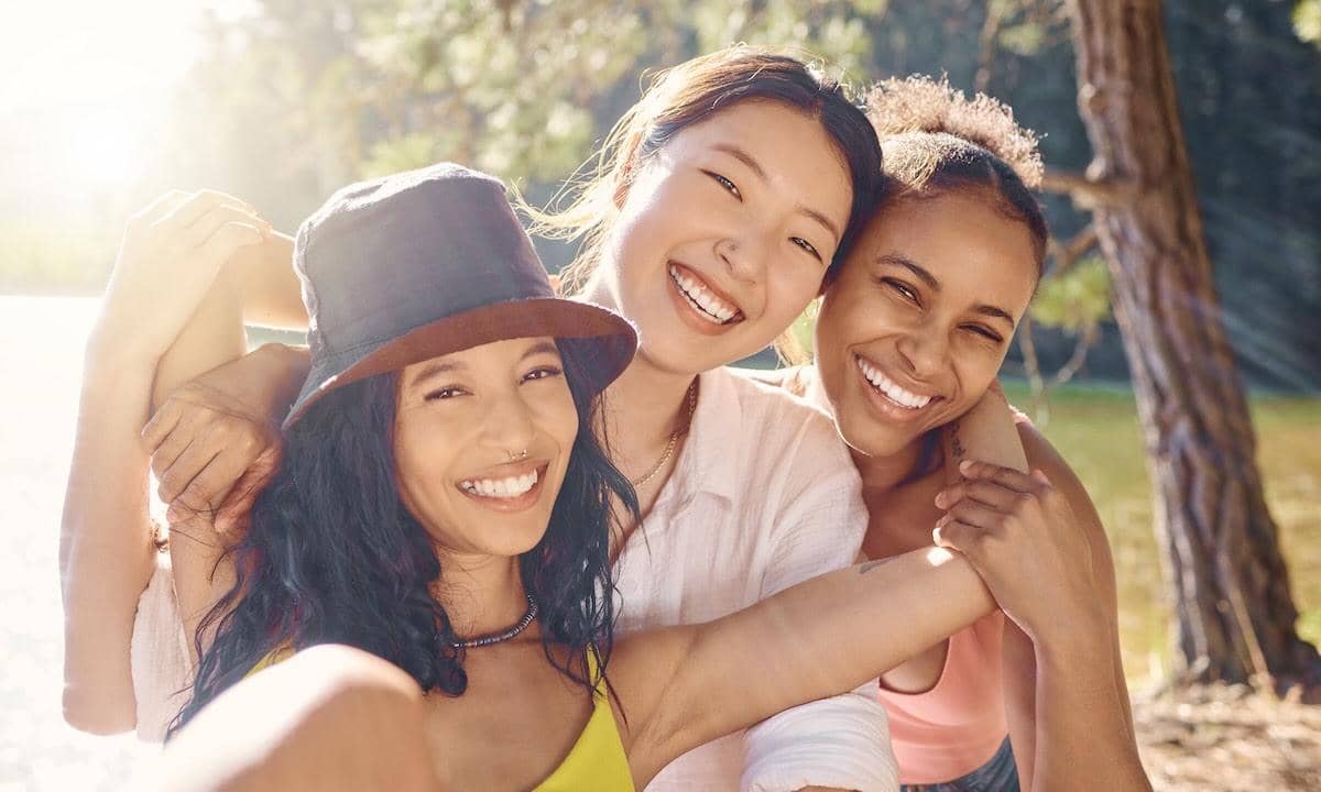 Shot of a diverse group of friends sitting together and taking a selfie while camping in the woods.