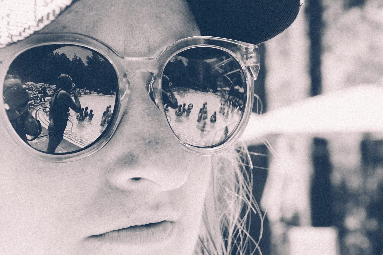 person with sunglasses reflecting a busy swimming pool