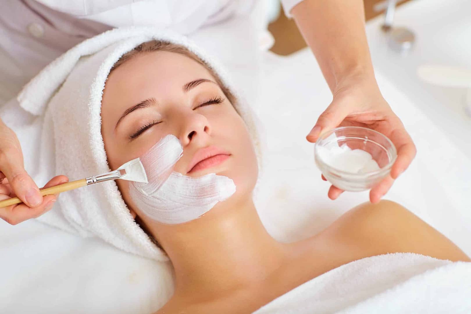 Woman having facial mask spread onto face